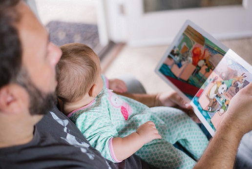 A father reading a picture book to a baby sitting on his knee